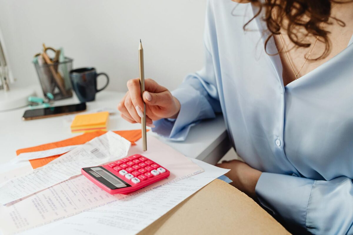 Bookkeeping - The Foundation of Financial Success for UK SMEs. A woman is calculating expenses using a calculator and papers at her desk.