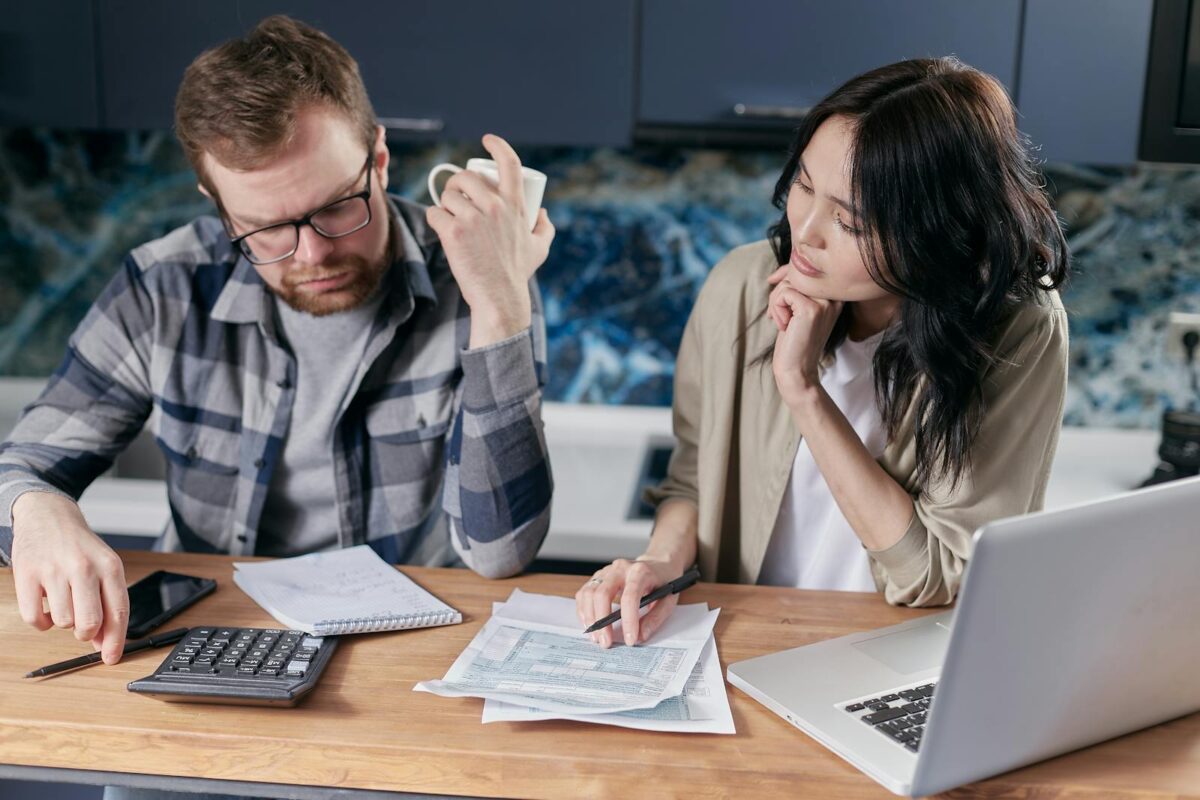 A couple reviews bills and documents on a laptop while discussing household finances. family tax