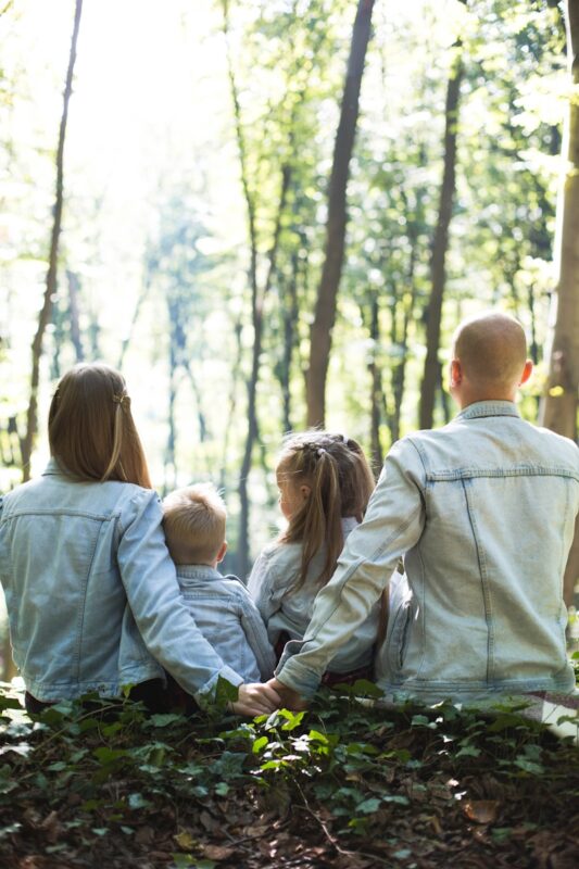 man and woman holding hands together with boy and girl looking at green trees during day. family tax