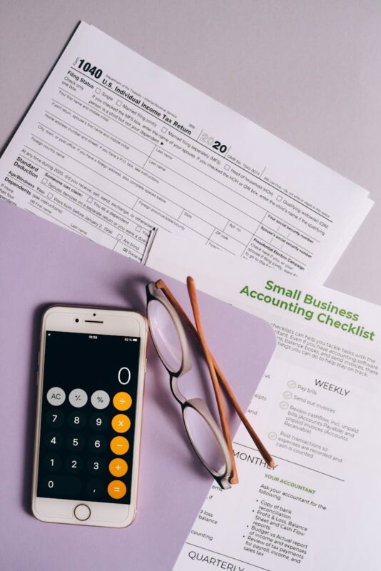 Flat lay of tax forms, checklist, smartphone, and glasses for small business accounting.HMRC Self Assessment Deductible Expenses